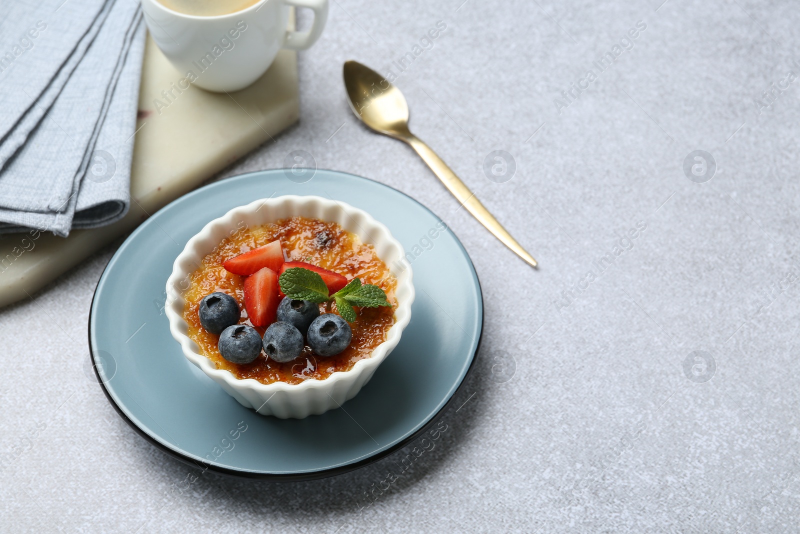 Photo of Delicious creme brulee with berries and mint in bowl served on grey textured table. Space for text