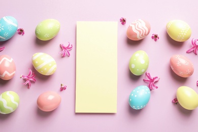 Flat lay composition with painted Easter eggs and blank card on color background, space for text