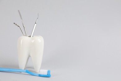 Photo of Tooth shaped holder with set of dentist's tools and brush on light grey background. Space for text