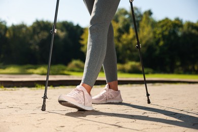 Photo of Woman practicing Nordic walking with poles in park on sunny day, closeup