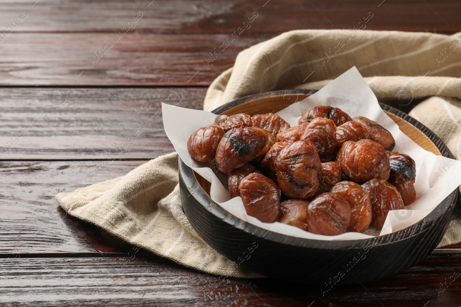 Photo of Roasted edible sweet chestnuts in bowl on wooden table, space for text