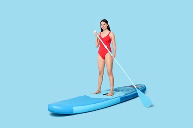 Happy woman with paddle on SUP board against light blue background