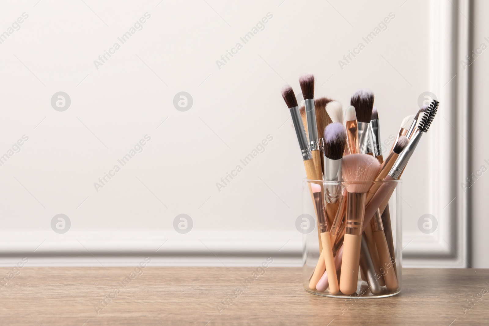 Photo of Set of professional makeup brushes on wooden table near white wall, space for text