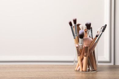 Set of professional makeup brushes on wooden table near white wall, space for text