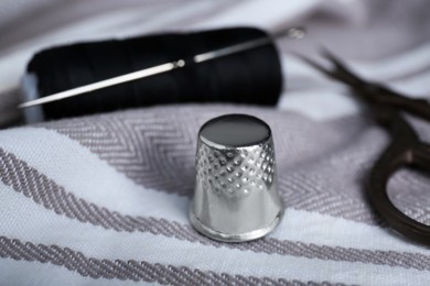 Photo of Silver thimble on striped cloth, closeup. Sewing accessory
