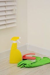 Photo of Spray bottle of cleaning product, rubber gloves and brush indoors