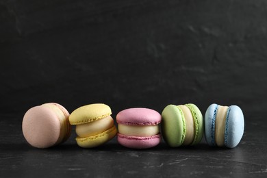 Delicious colorful macarons on black table, space for text