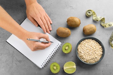 Photo of Woman developing diet plan at grey table with products and measuring tape, top view