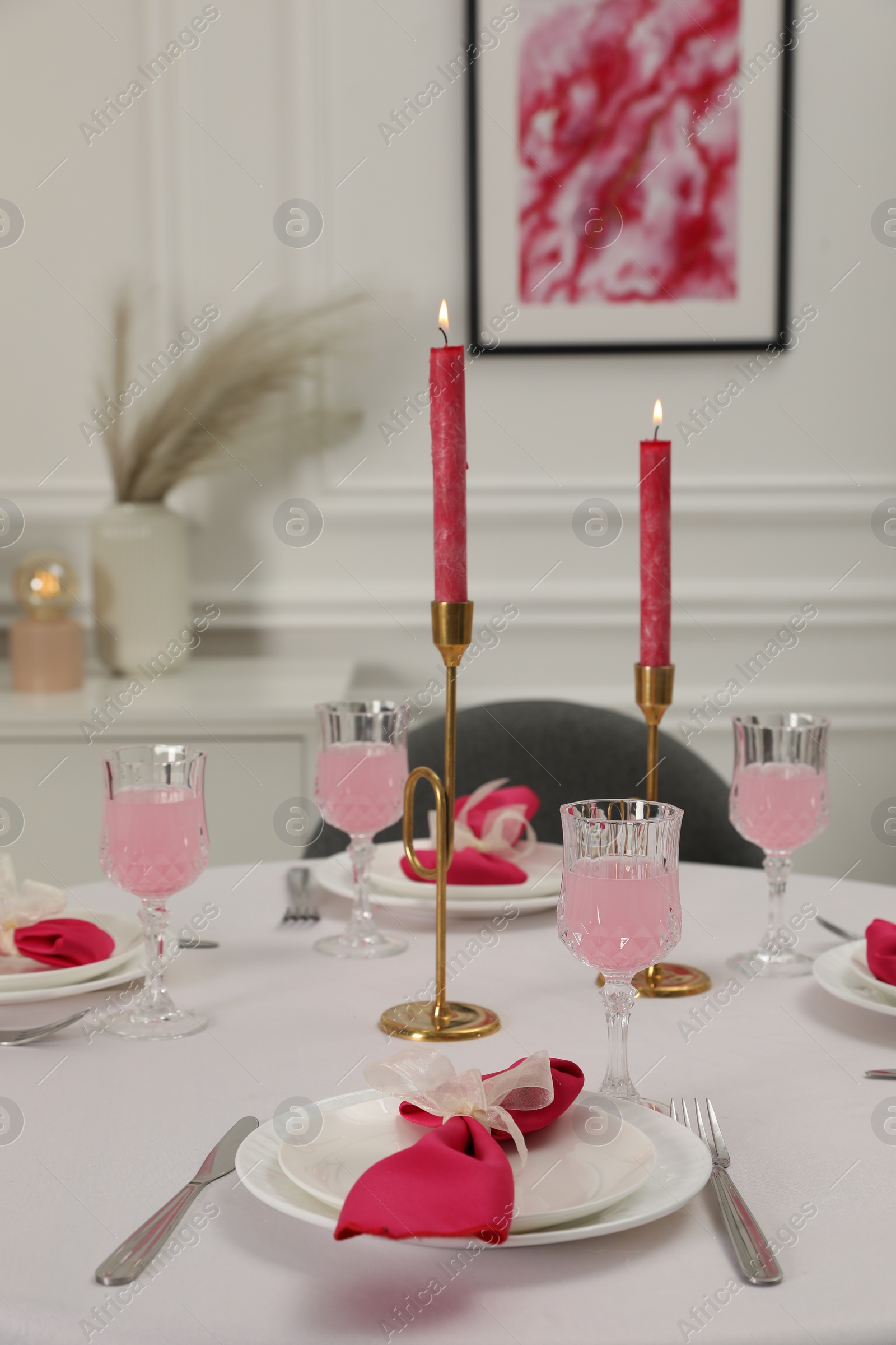 Photo of Color accent table setting. Glasses, plates, burning candles and pink napkins on table in dining room