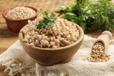 Photo of Delicious pearl barley with parsley in bowl on table, closeup