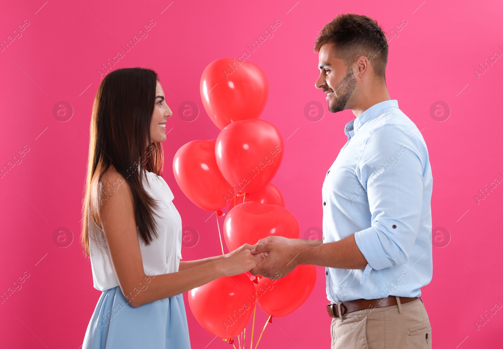 Photo of Young couple and air balloons on pink background. Celebration of Saint Valentine's Day