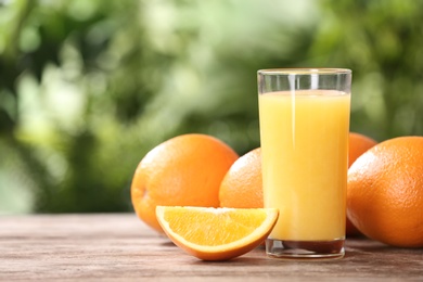 Photo of Glass of fresh juice and oranges on wooden table. Space for text