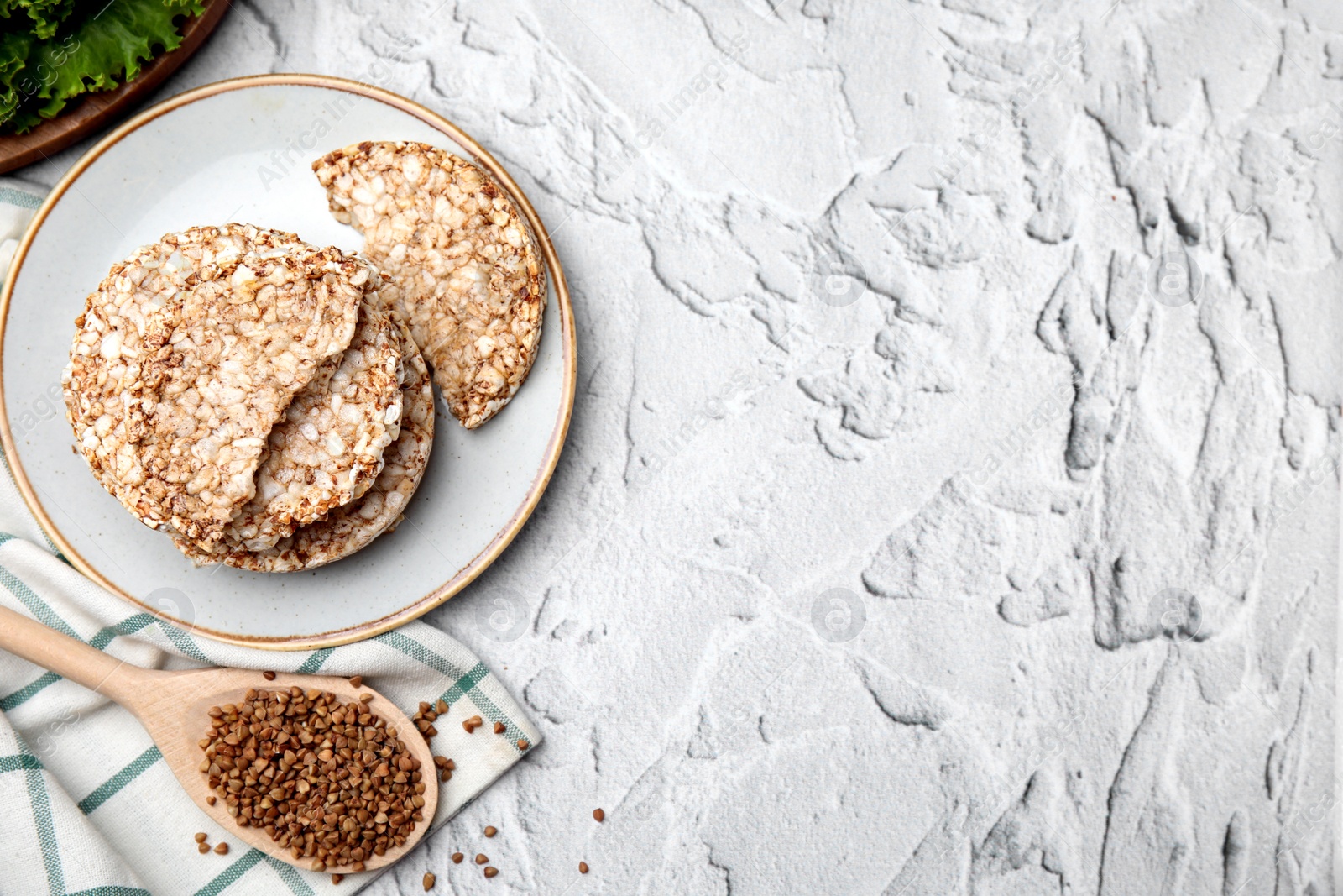 Photo of Crunchy buckwheat cakes and spoon with cereal on white textured table, flat lay. Space for text