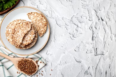 Photo of Crunchy buckwheat cakes and spoon with cereal on white textured table, flat lay. Space for text