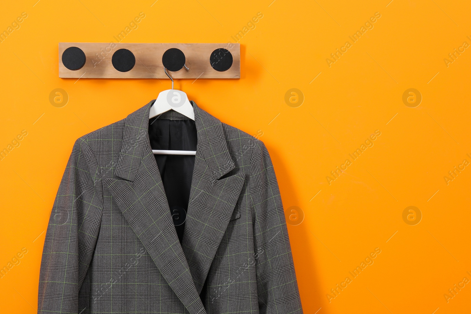 Photo of Hanger with stylish jacket on orange wall, space for text