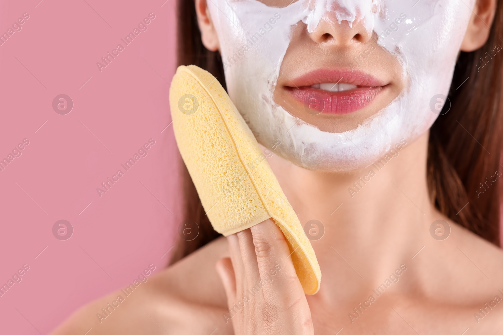 Photo of Young woman removing face mask with sponge on pink background, closeup