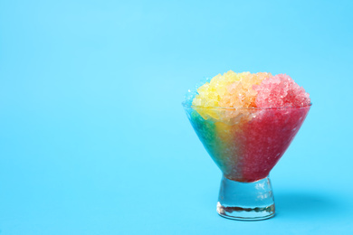 Photo of Rainbow shaving ice in glass dessert bowl on light blue background, space for text