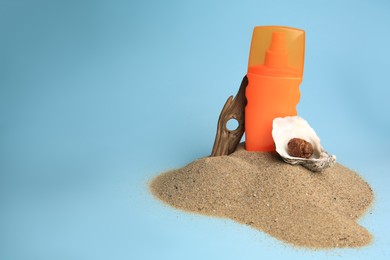 Sand with bottle of sunscreen, tree bark and seashells against light blue background, space for text. Sun protection