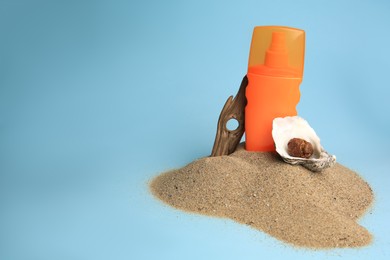 Photo of Sand with bottle of sunscreen, tree bark and seashells against light blue background, space for text. Sun protection