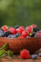 Photo of Bowl with different fresh ripe berries and mint on wooden table outdoors