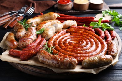 Photo of Different delicious sausages with herbs on black wooden table. Assortment of beer snacks