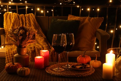 Glasses of wine, burning candles and autumn decor on outdoor terrace in evening