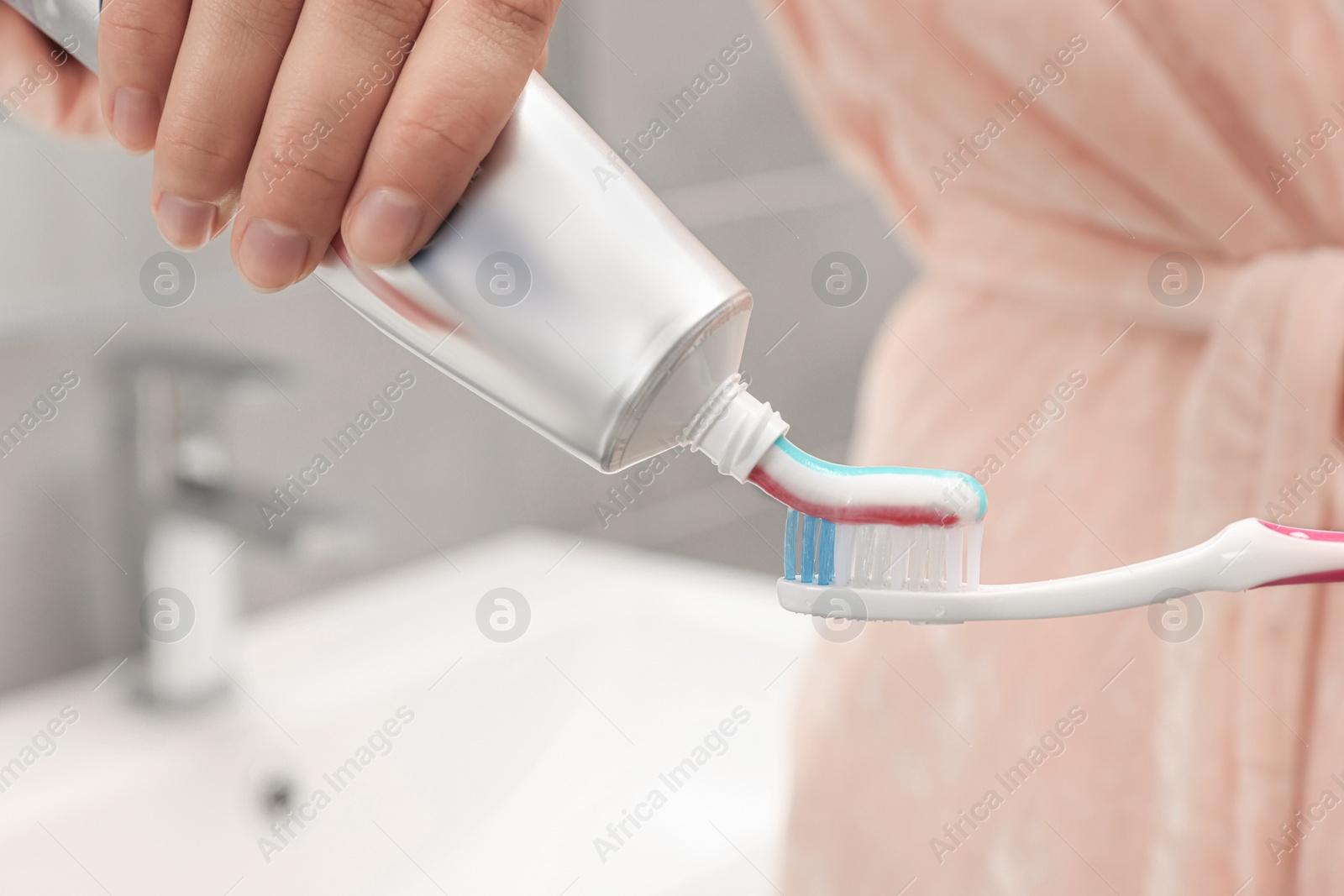 Photo of Woman applying toothpaste on brush in bathroom, closeup