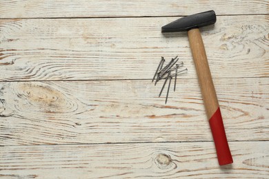 Photo of New hammer and metal nails on wooden table, flat lay. Space for text