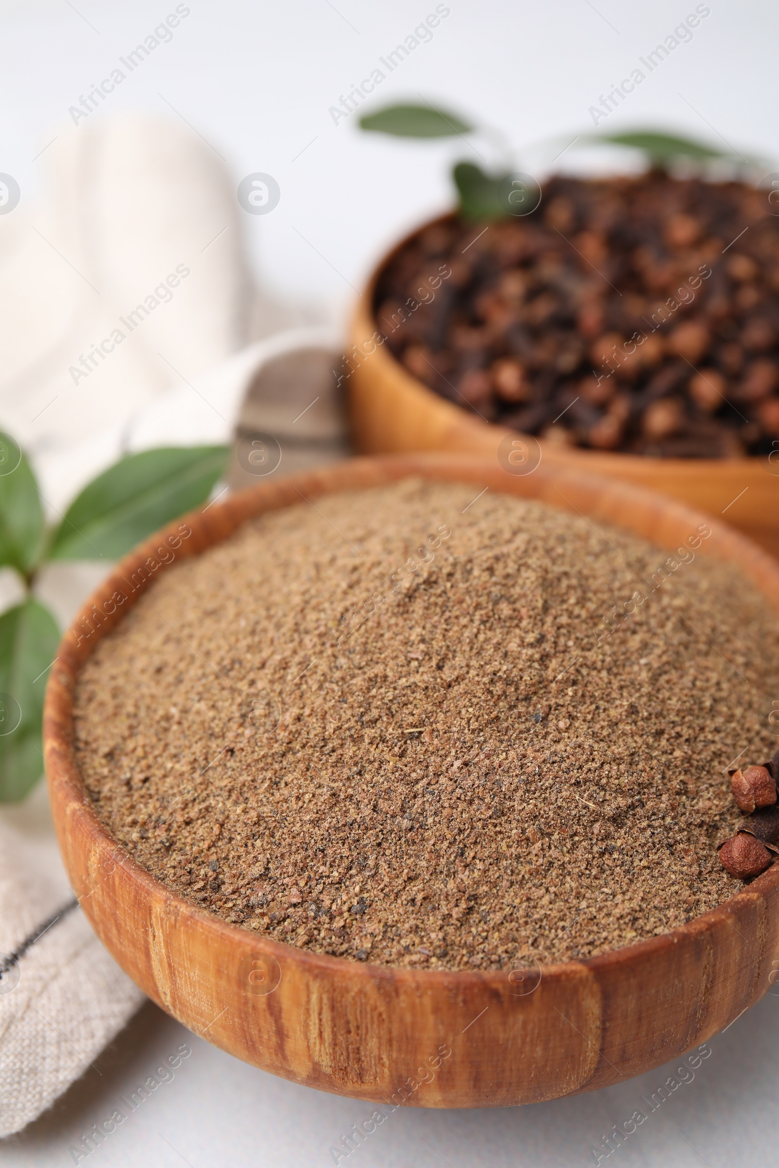 Photo of Aromatic clove powder and dried buds in bowls on white table, closeup