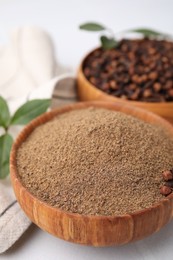 Aromatic clove powder and dried buds in bowls on white table, closeup