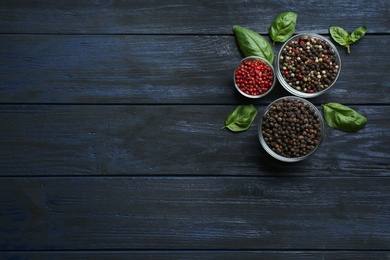 Photo of Different peppercorns in bowls on dark wooden table, top view. Space for text
