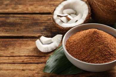 Photo of Natural coconut sugar in bowl on wooden table, space for text