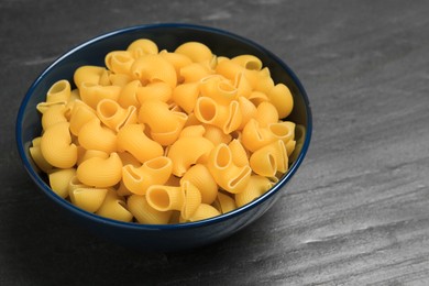 Raw macaroni pasta in bowl on grey table, closeup