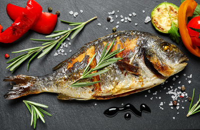 Photo of Delicious roasted fish and vegetables on black table, flat lay