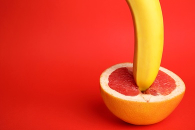 Photo of Fresh grapefruit and banana on red background, space for text. Sex concept
