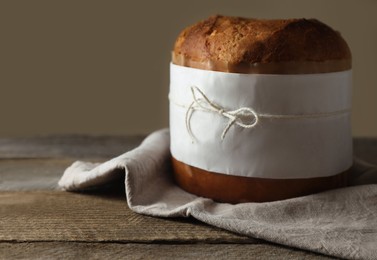 Photo of Delicious Panettone cake wrapped in parchment paper on wooden table, space for text. Traditional Italian pastry