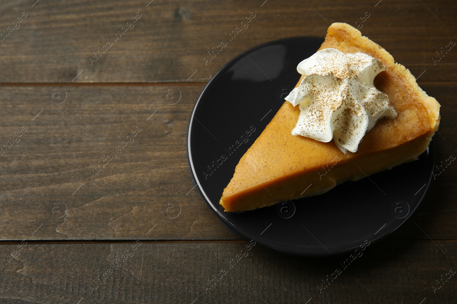 Photo of Piece of delicious pumpkin pie with whipped cream on wooden table, above view. Space for text