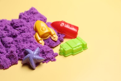 Violet kinetic sand and plastic toys on beige background, space for text