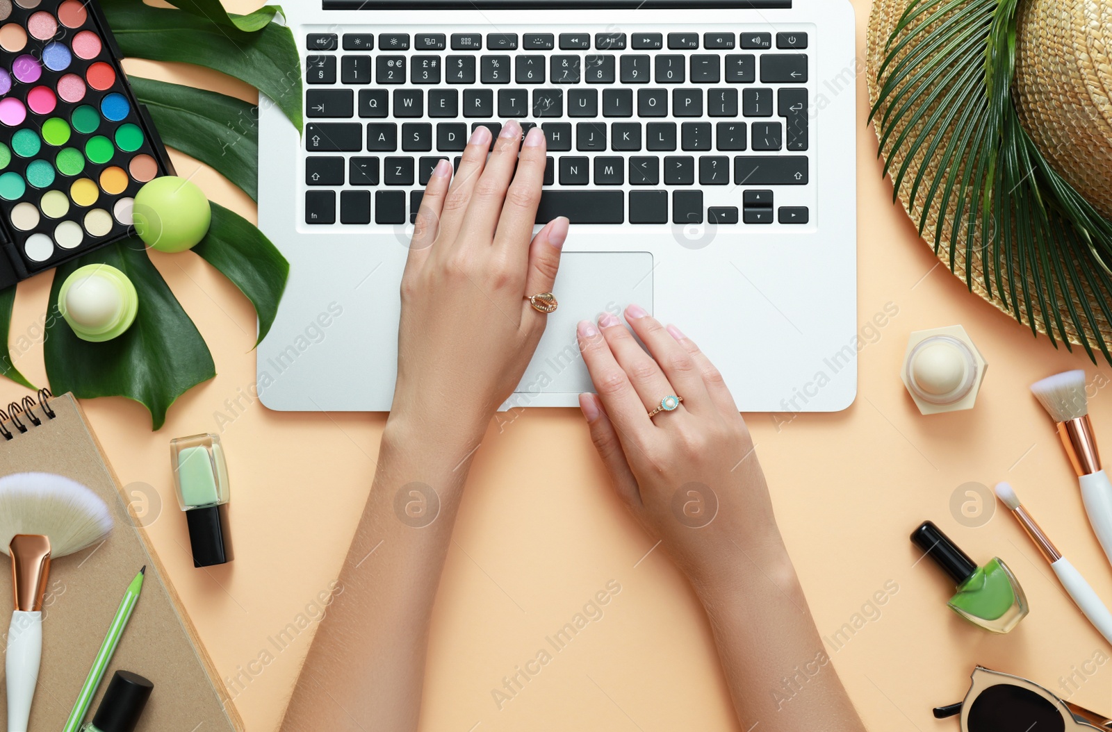 Photo of Young beauty blogger working with laptop near accessories on light orange background, top view