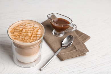 Composition with glass of caramel macchiato and gravy boat with sauce on wooden table