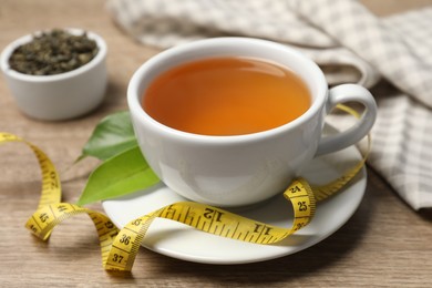 Photo of Cup of herbal diet tea and measuring tape on wooden table, closeup. Weight loss concept