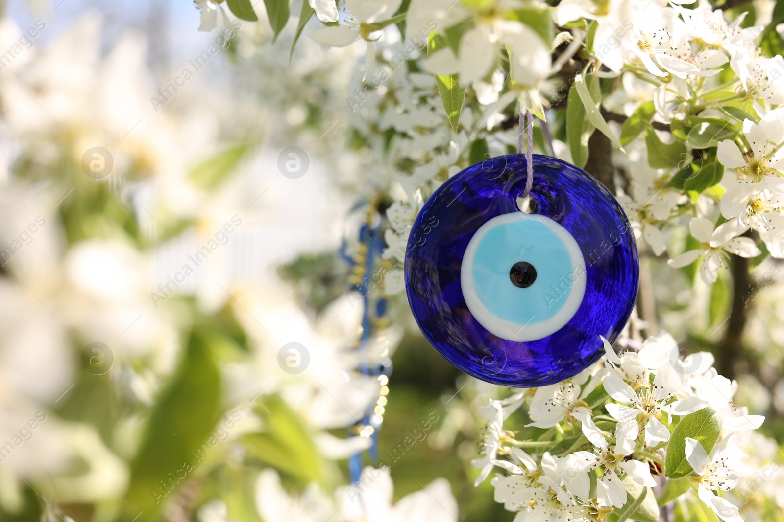Photo of Eye bead against evil eye on blossoming tree outdoors, closeup. Space for text