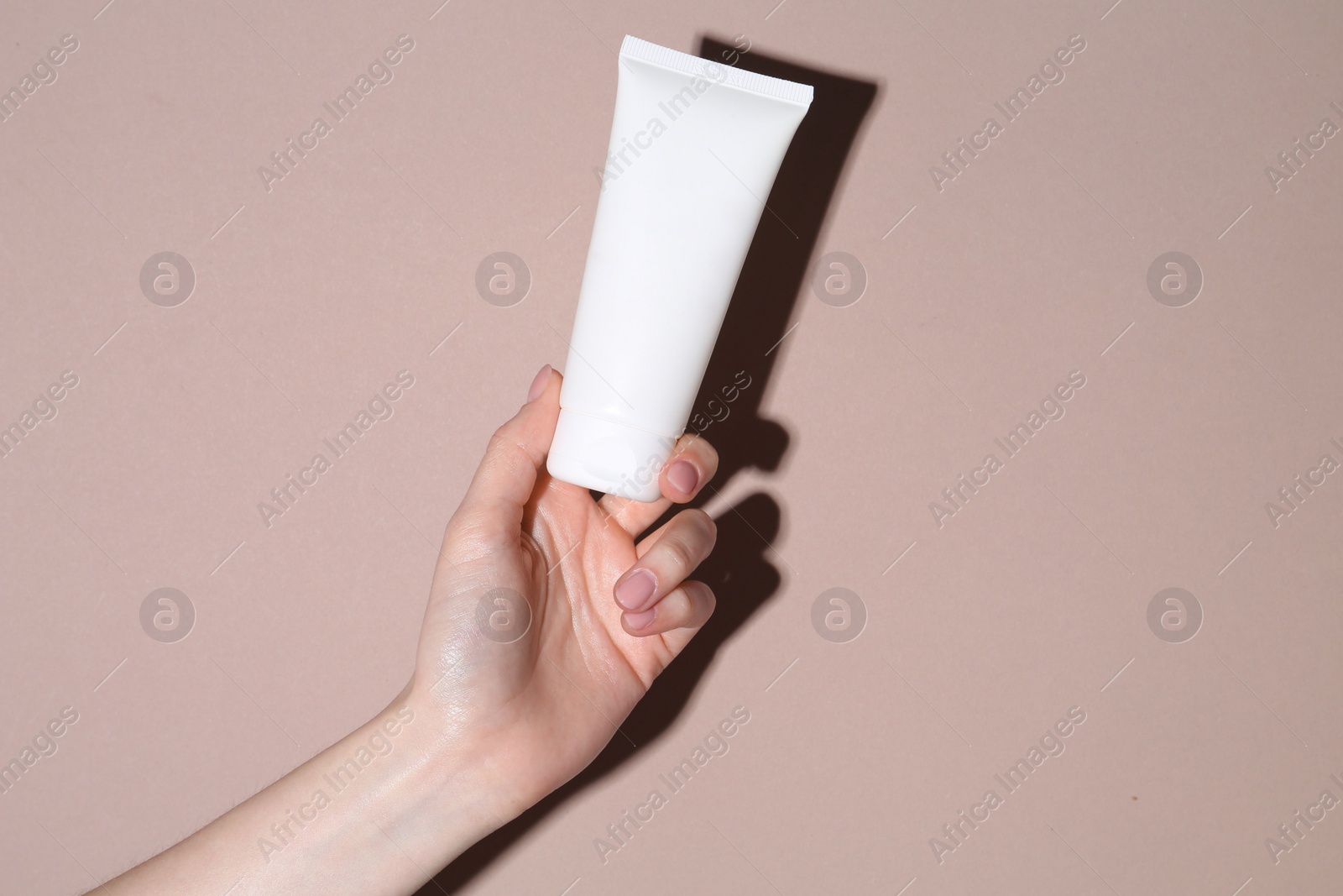 Photo of Woman with tube of cream on beige background, closeup. Space for text