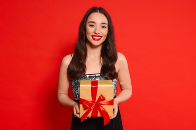Photo of Beautiful young woman with Christmas gift on red background