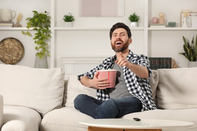 Photo of Laughing man watching TV with popcorn on sofa at home, space for text
