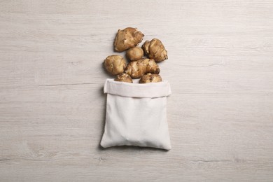 Photo of Bag with many Jerusalem artichokes on white wooden table, flat lay