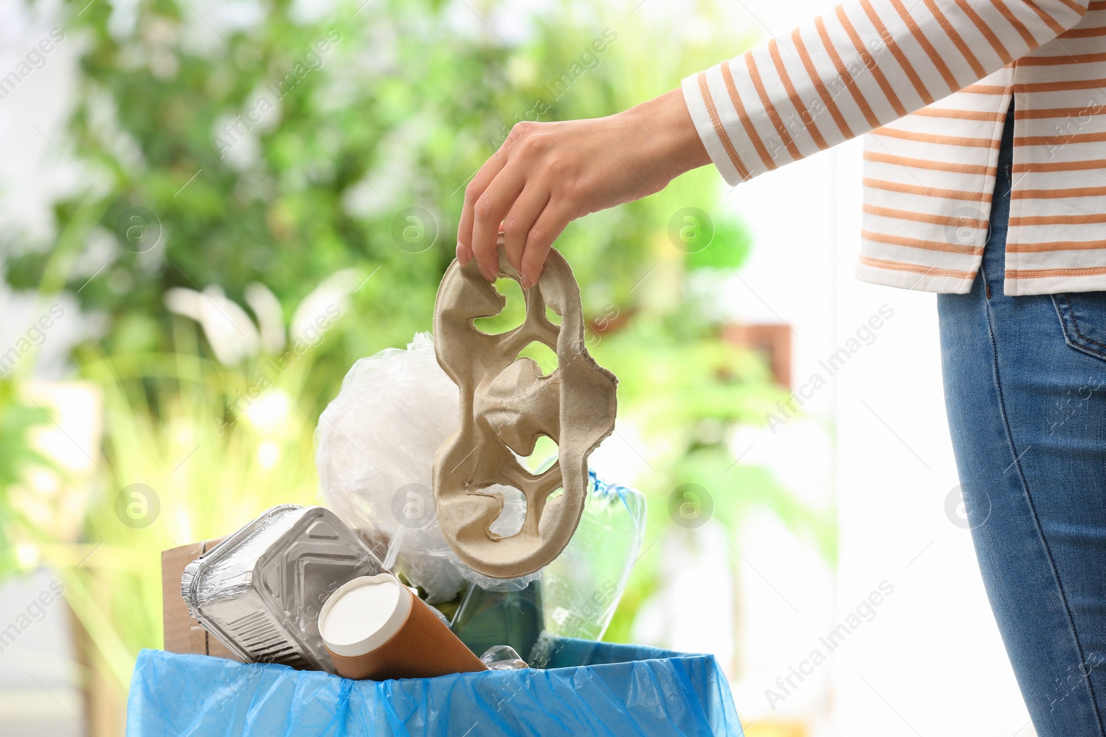 Photo of Woman putting paper garbage into trash bin on blurred background, closeup. Recycling problem