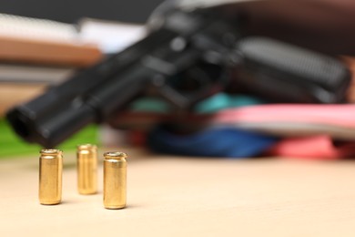 Photo of Gun and school stationery on wooden table, focus of bullets. Space for text