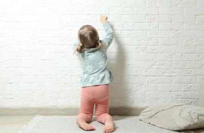 Little girl drawing on white brick wall indoors, back view. Child`s art