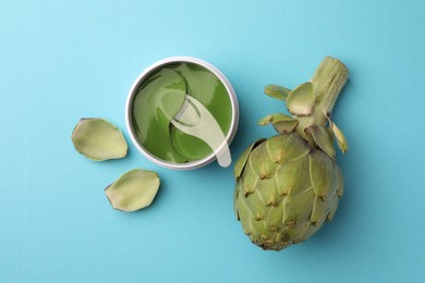 Package of under eye patches and artichoke on light blue background, flat lay. Cosmetic product